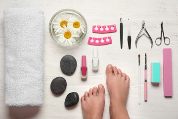 Feet of young woman and set for pedicure on wooden background, top view