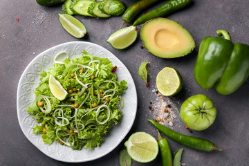 Plate with healthy vegetable salad and ingredients on grey background