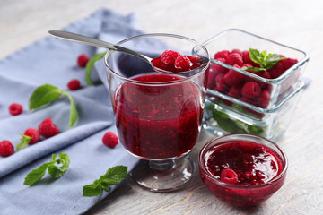 Glass and bowls with tasty raspberry jam on wooden table