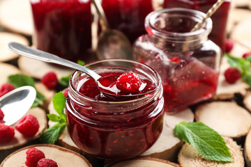 Glass jar with tasty raspberry jam on wooden surface