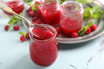 Glass jar with tasty raspberry jam on light table