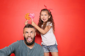 Funny portrait of father and his little daughter with lollipops on color background