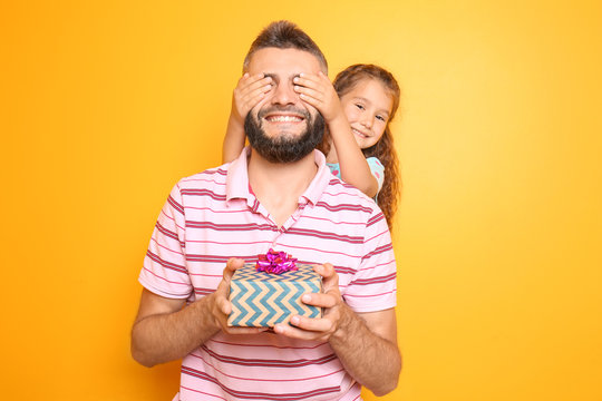 Little girl giving present to her father on color background