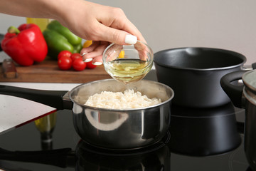 Woman pouring oil into saucepan with boiled rice in kitchen