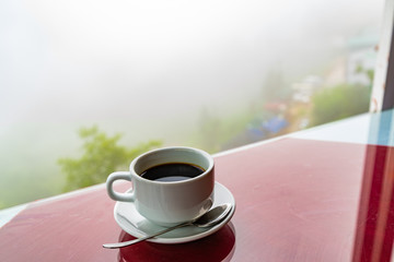 Black coffee in white cup by the window background of mountains fog and mist on forest In the morning. Feels good.