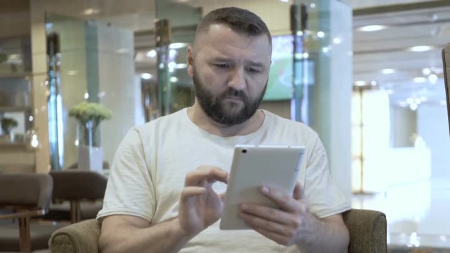 Handsome man sitting in the hotel's cafe and browsing internet on tablet
