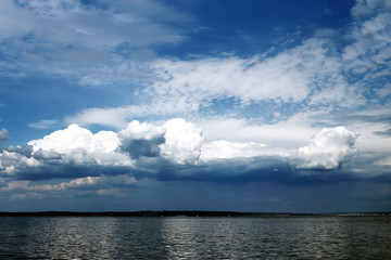 Bright clouds in the sky. Soon the storm will begin. Dark water on the river and the distant shore.