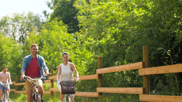 people, leisure and lifestyle concept - happy young friends riding fixed gear bicycles at country or summer park