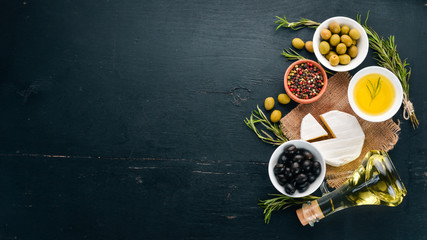 Olives, olive oil, cheese and spices. On a black wooden background. Free space for text.