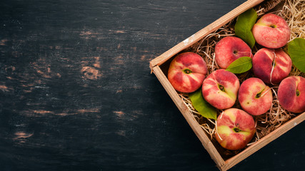 Flat peach in a wooden box. On a black wooden background. Top view. Free space for your text.
