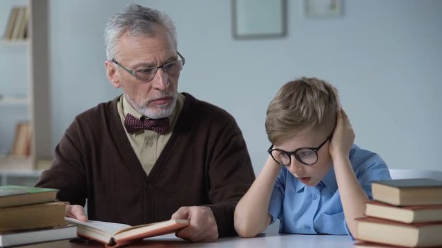 Grandfather reading aloud book, little boy looks bored, generation gap problem