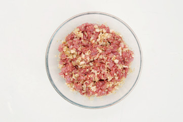 In a deep bowl of chopped meat with onions, spices and pieces of fat. White background. Close-up. View from above.
