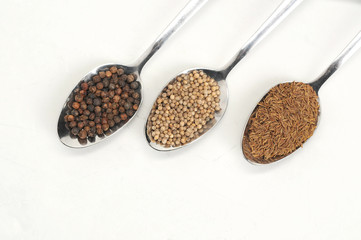 Cumin, cardamom, black pepper peas in spoons. White background. Close-up. View from above.