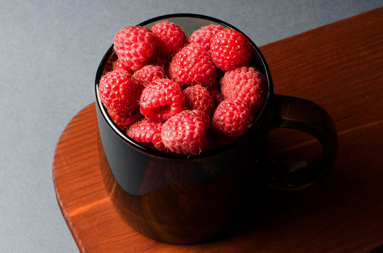 Lots of red ripe raspberries in a glass Cup. Wooden background