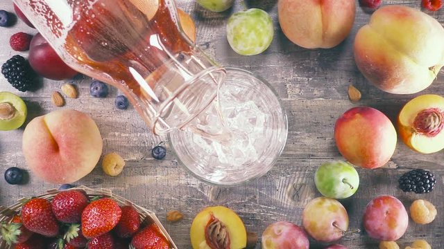 Slow motion from the decanter pour into a glass of ice fruit tea on the background of fruit top view