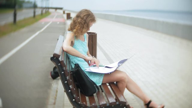 A woman sitting on a bench on the beach using a laptop