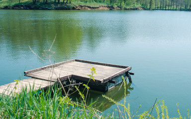 Naklejka premium Small wooden wharf made of planks over the pond water for fishermen and boats.