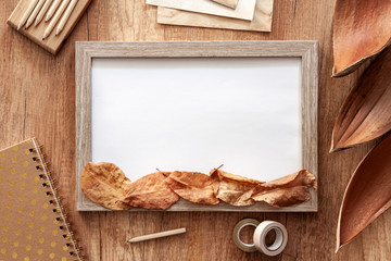 Autumn leaves on a mockup frame, exercise book, pencils and decorations on a wooden table