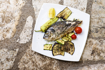 Delicious roast bream or dorade fish on stone background. Fish with aromatic herbs, lemon, spices...