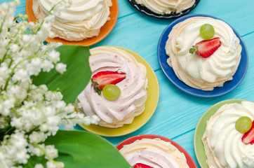 Strawberry pavlova cake nests, meringue decoration on wood table with lily of the valley flowers.