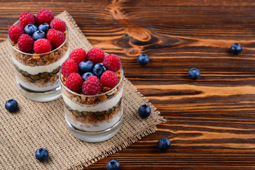 Healthy blueberry and raspberry parfait in a glass on a rustic brown wood background. Two portions. Space for text or design.