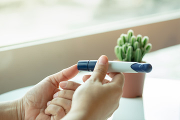 Close up of woman hands using lancet on finger to check blood sugar level by Glucose meter. Medicine, diabetes, glycemia, health care concept.