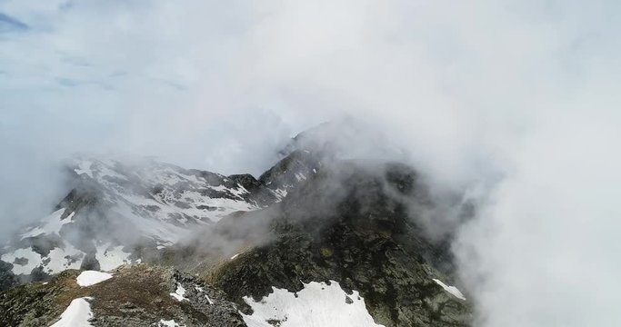 Forward aerial top view over cloudy rocky snowy mountain in sunny day with clouds.Italian alps mountains in summer with wild windy weather outdoor nature establisher.4k drone flight establishing shot