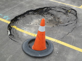 Constructions at unexpected sink hole in public parking lot with traffic cone. This accident causes...