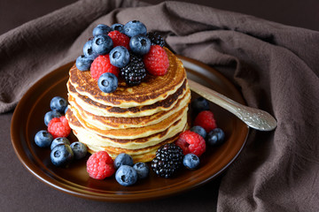 Stack of pancakes with fresh blueberry, raspberry and blackberry on brown plate