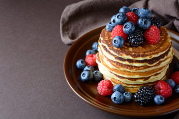 Stack of pancakes with fresh blueberry, raspberry and blackberry on brown plate