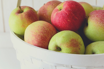 White basket with red and green apples on front of white wooden wall. Harvest concept