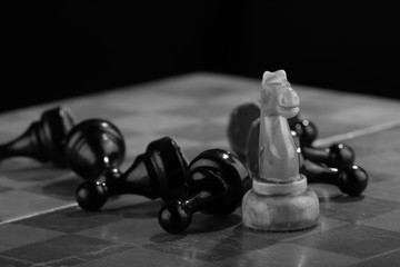 White chess knight swept through the army of enemy pawns on an old scratched chessboard. Rush attack. Black Army is defeated. Concept of conflict and active actions © alexstepanov