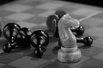 White chess knight swept through the army of enemy pawns on an old scratched chessboard. Rush...