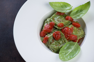 Spinach ravioli with tomato sauce and fresh green basil served in a white plate, close-up, top view