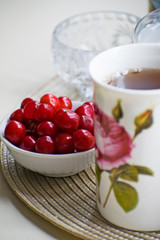 Red juicy and ripe cherries in a white bowl and a cup of tea on a table