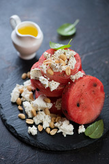 Fresh round watermelon slices with feta cheese and nuts on a stone slate tray, studio shot
