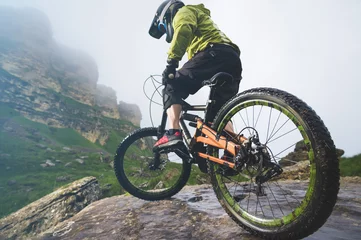 Foto op Plexiglas Legs of bicyclist and rear wheel close-up view of back mtb bike in mountains against background of rocks in foggy weather. The concept of extreme sports © yanik88