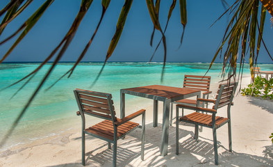 table and chairs on the ocean beach on a tropical island in the Maldives.Tables and chairs in the shadow of palm tree on a tropical island.