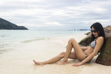 Fototapeta na wymiar Young slim Asian woman wearing bikini lying on sea rocks, sea and waves as background. Beach and natural in summer.