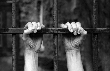 Hands of the prisoner on a steel lattice close-up, black and white