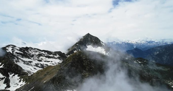 Forward aerial top view over cloudy rocky snowy mountain in sunny day with clouds.Italian alps mountains in summer with wild windy weather outdoor nature establisher.4k drone flight establishing shot