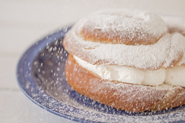 Cream puff filled with wipped cream. Icing sugar falling.