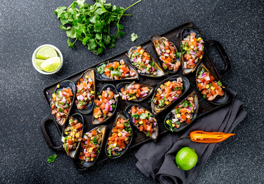 PERUVIAN FOOD. Choros a la chalaca. Big mussels, choros zapatos seasoned with purple onion, tomatoes, corn and lemon. Top view, black background. Traditional peruvian dish