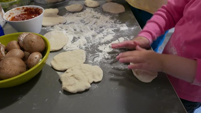 Little girl kneading dough for little pizzas
