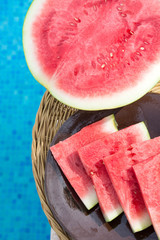 Ripe Juicy Seedless Halved Watermelon Slices Wedges on Plate on Rattan Table by Swimming Pool. Sunlight. Seaside Vacation Relaxation Wanderlust Summer Vibes. Authentic Atmosphere. Lifestyle. Poster