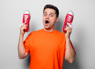 Young handsome man in orange t-shirt with red gumshoes. Studio image on white background