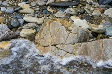 pebble stones on the sea beach, the rolling waves of the sea with foam