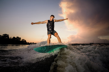 Young athletic man wakesurfing down the river waves