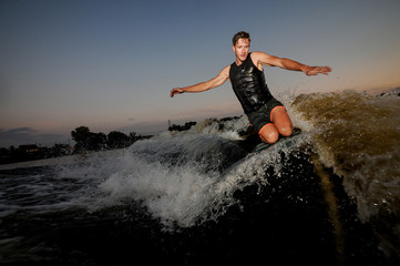Muscular young man wakesurfing down the river waves