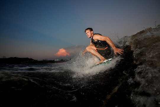 Young and active man riding on wakesurf down the river during summer sunset